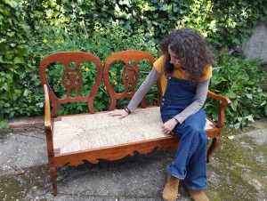 Jana Úbeda revisando un banco restaurado con asiento de anea tejido a mano.